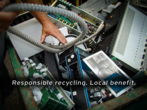 A person’s hands sorting through a large bin filled with dismantled electronic components and devices. Overlaid text reads, "Responsible recycling. Local benefit," emphasizing the importance of community-oriented e-waste recycling.